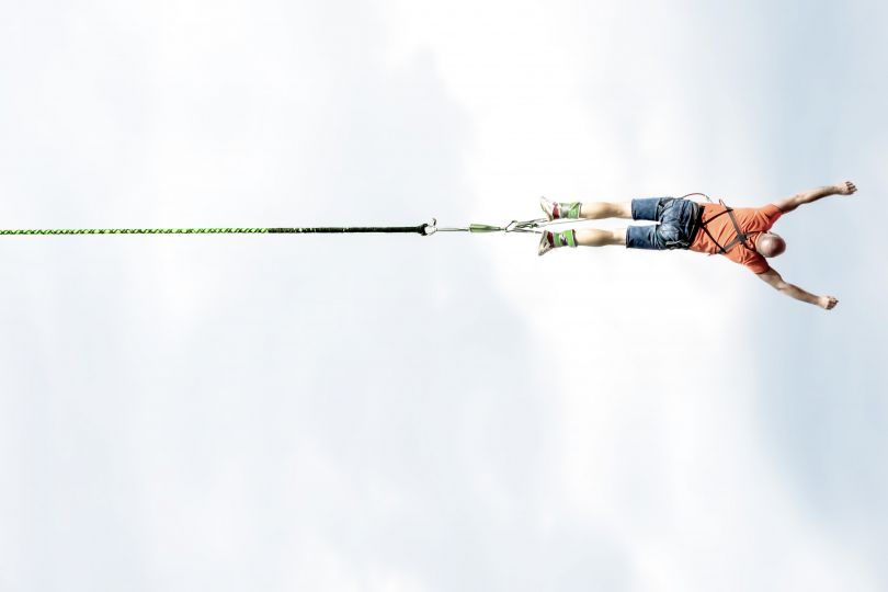 Ein Mann springt an einem Bungee-Seil waagrecht ins Bild.