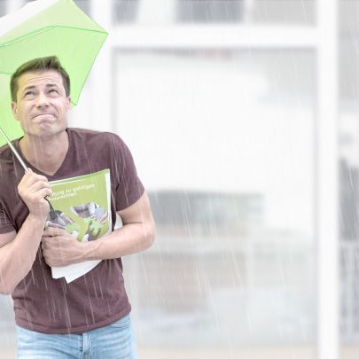 Ein junger Mann hält in einer Hand einen SFG-Folder zum Schutz von geistigem Eigentum, in der anderen einen grünen Schirm, um sich vor dem Regen zu schützen.