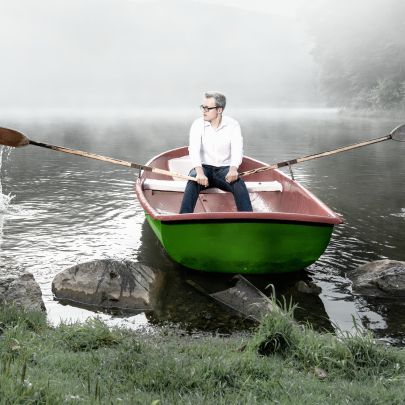 Ein junger Mann in weißem Hemd startet ein grünes Ruderboot in einem nebelverhangenen See