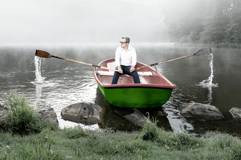 Ein junger Mann in weißem Hemd startet ein grünes Ruderboot in einem nebelverhangenen See