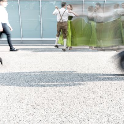 Paar in Tracht tanzt vor moderner urbaner Kulisse.