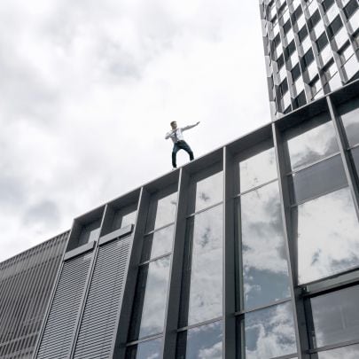 Ein junger Mann in Turnschuhen, Hemd und Krawatte steht auf einem Hochhaus in dynamischer Pose.