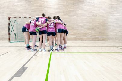 Eine Damen-Handballmannschaft beim Time-out steht in einer Gruppe und steckt die Köpfe zusammen.