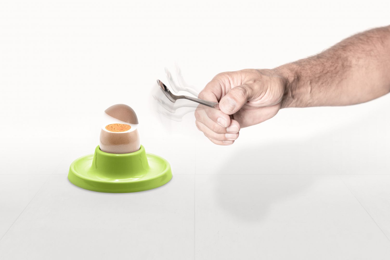 Hand schlägt mit Löffel gekochtes Ei auf. Ei springt mit gerader Bruchstelle auf.