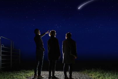 Familie steht in der Nacht auf Weg und beobachtet eine Sternschnuppe