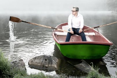 Mann rudert in Boot auf einem See vom Ufer weg