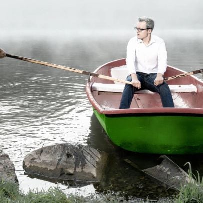 Mann rudert in Boot auf einem See vom Ufer weg