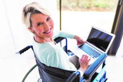 Frau sitzt im Rollstuhl mit Laptop am Schoß