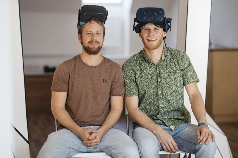 Zwei Männer sitzen auf Stühlen mit Virtal-Reality-Brillen auf der Stirn.