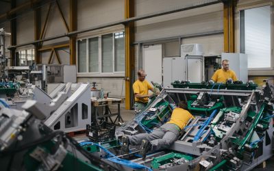 Drei Männer in gelben Shirts arbeiten an Maschine, einer der drei liegt auf dem Bauch auf der Maschine