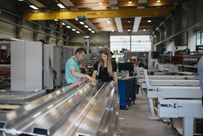 Florian Hampel zeigt Sigrid Merth in Produktionshall lange Metallteile
