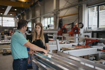 Florian Hampel zeigt Sigrid Merth in Produktionshall lange Metallteile