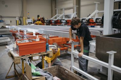 Zwei junge Männer arbeiten in Produktionshalle an langen Metallkonstruktionen