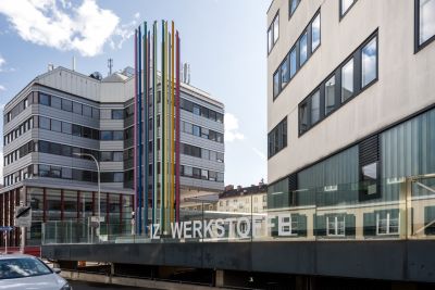 Zwei moderne Gebäude, bunte Stäbe, Schriftzug IZ-WERKSTOFFE
