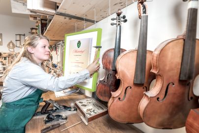 Frau hängt Meisterbrief in Instrumentenbauer-Werkstatt an die Wand