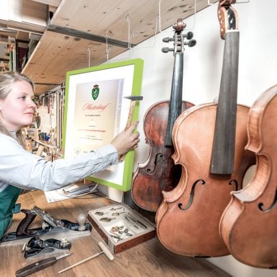 Frau hängt Meisterbrief in Instrumentenbauer-Werkstatt an die Wand